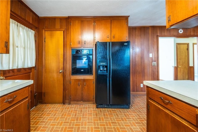 kitchen featuring black appliances, wooden walls, brown cabinetry, and light countertops