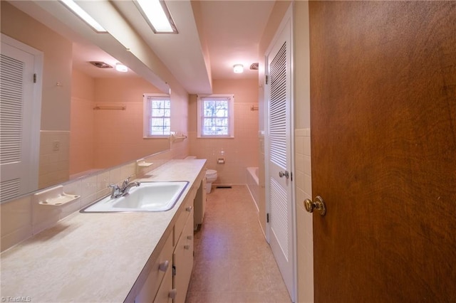 bathroom with vanity, a closet, walk in shower, tile walls, and toilet