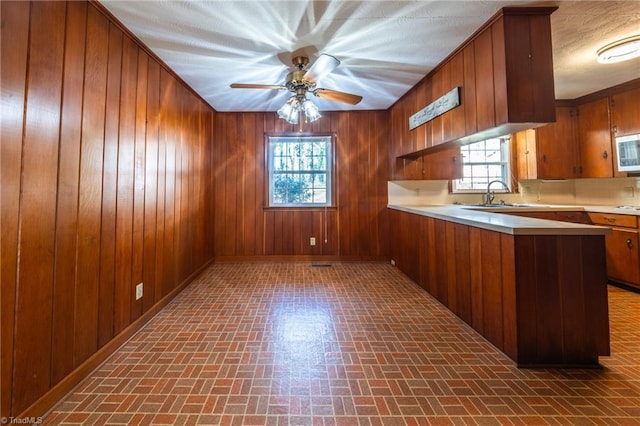 kitchen with wood walls, light countertops, brown cabinets, a peninsula, and a sink