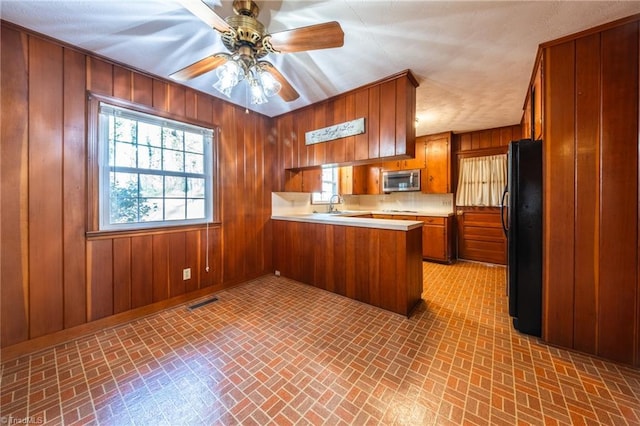 kitchen featuring brown cabinetry, a healthy amount of sunlight, a peninsula, freestanding refrigerator, and stainless steel microwave