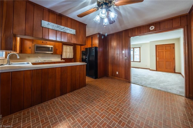 kitchen with a ceiling fan, a sink, stainless steel microwave, freestanding refrigerator, and wood walls