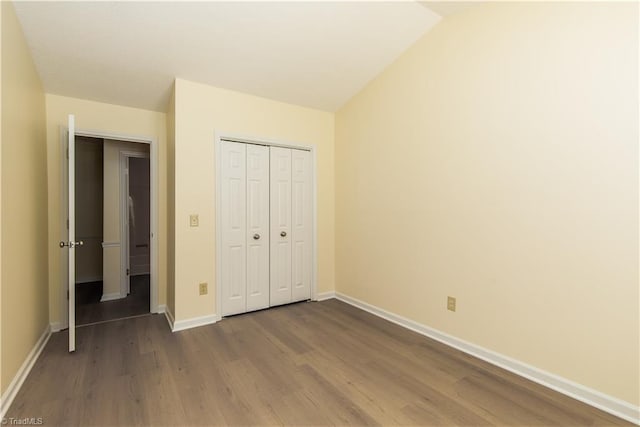 unfurnished bedroom with vaulted ceiling, dark wood-type flooring, a closet, and baseboards