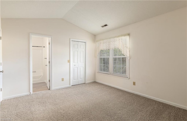 unfurnished bedroom featuring lofted ceiling, connected bathroom, carpet flooring, visible vents, and baseboards