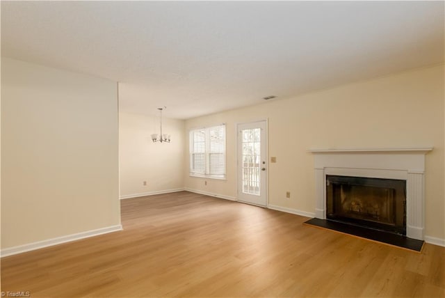 unfurnished living room featuring a chandelier, light wood finished floors, a fireplace, and baseboards