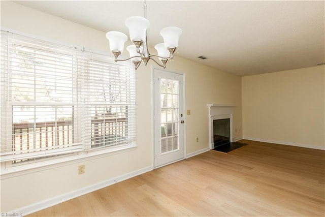 unfurnished dining area featuring a fireplace with flush hearth, a chandelier, baseboards, and wood finished floors