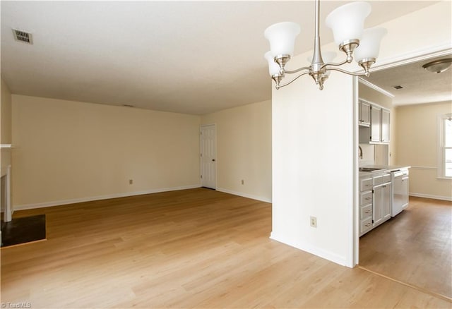 unfurnished dining area featuring a notable chandelier, light wood finished floors, visible vents, a sink, and baseboards