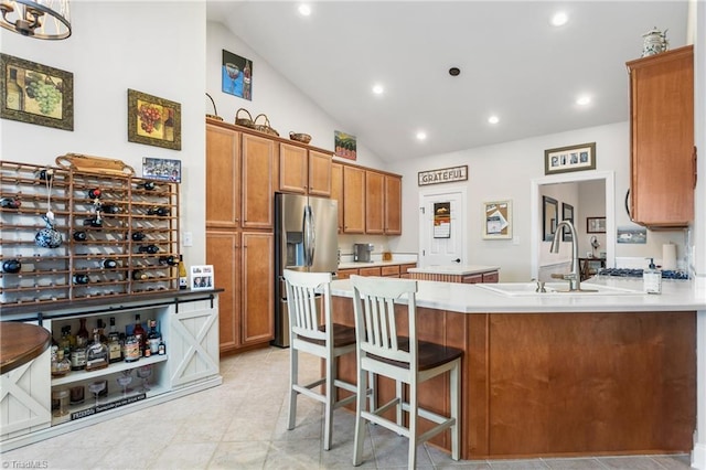 kitchen featuring lofted ceiling, kitchen peninsula, a kitchen bar, sink, and stainless steel fridge