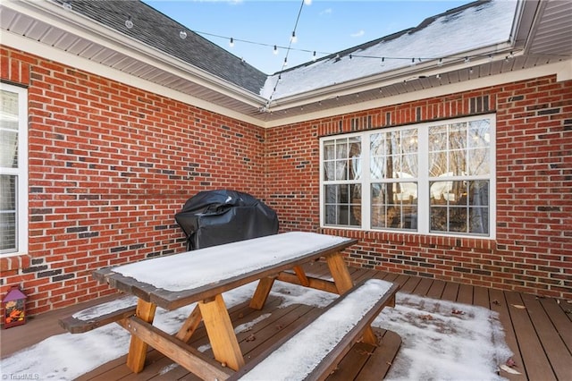 snow covered patio with grilling area and a wooden deck