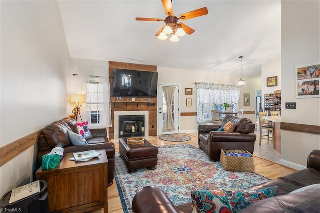 living room with ceiling fan, vaulted ceiling, a large fireplace, and light hardwood / wood-style floors