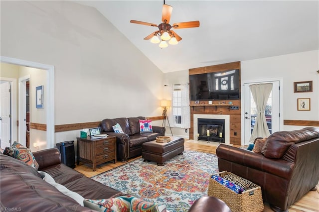 living room with ceiling fan, light wood-type flooring, a large fireplace, and high vaulted ceiling