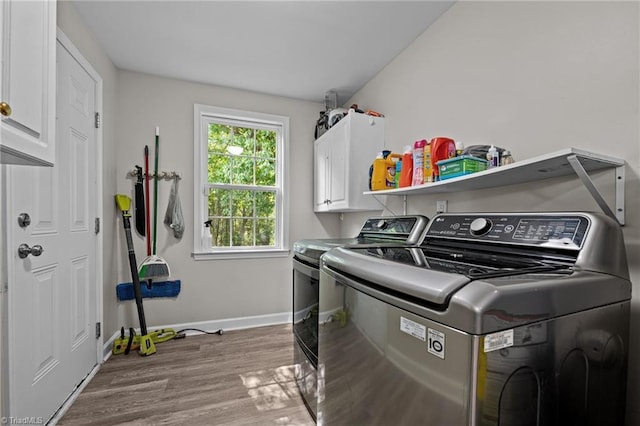 clothes washing area with baseboards, cabinet space, wood finished floors, and washing machine and clothes dryer