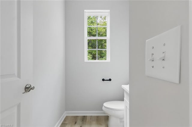 half bathroom featuring vanity, toilet, baseboards, and wood finished floors