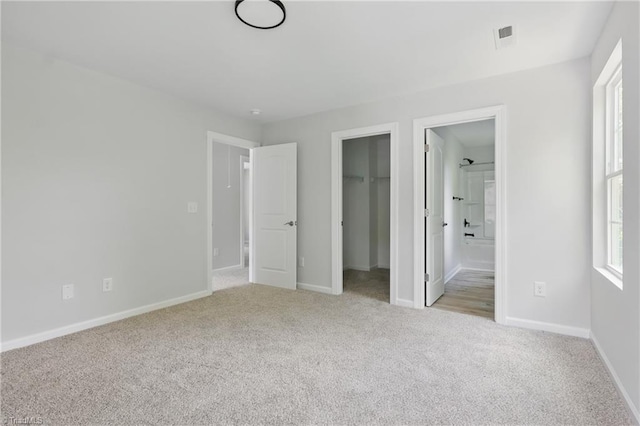 unfurnished bedroom featuring light colored carpet, a walk in closet, and baseboards