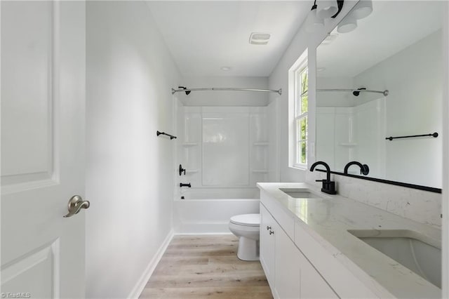 bathroom with toilet, wood finished floors, double vanity, baseboards, and shower / washtub combination