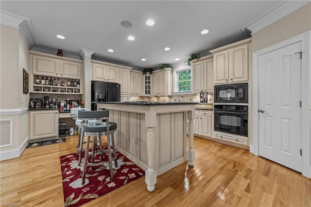 kitchen featuring black appliances, crown molding, cream cabinetry, a breakfast bar area, and light wood-style flooring