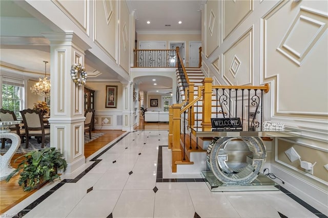 foyer featuring ornate columns, a decorative wall, stairs, inlaid floor details, and ornamental molding