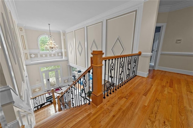 hall with a chandelier, an upstairs landing, ornamental molding, wood finished floors, and french doors