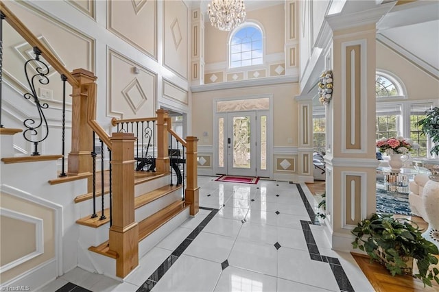 entrance foyer with a towering ceiling, a decorative wall, stairs, inlaid floor details, and a chandelier