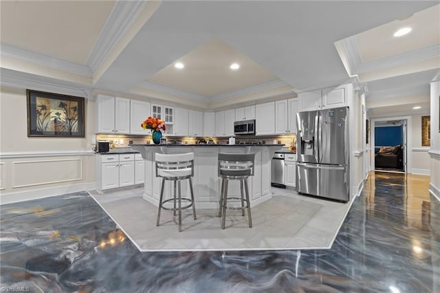 kitchen with appliances with stainless steel finishes, a tray ceiling, dark countertops, a kitchen bar, and white cabinets