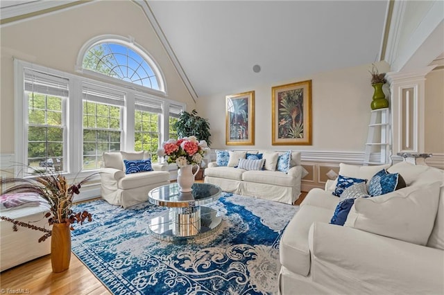 living room with a wainscoted wall, high vaulted ceiling, wood finished floors, and ornate columns