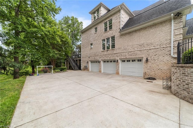 view of side of property with brick siding, an attached garage, driveway, stairway, and roof with shingles