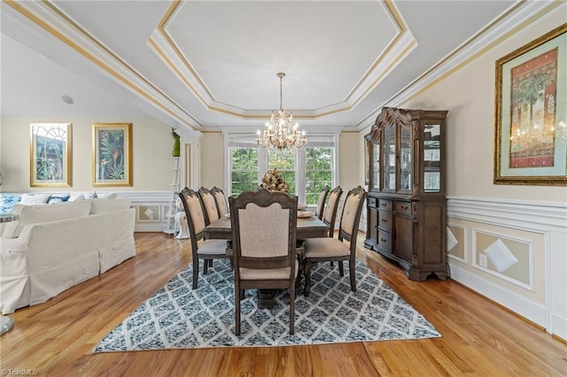 dining space featuring a chandelier, a decorative wall, a raised ceiling, crown molding, and light wood-style flooring