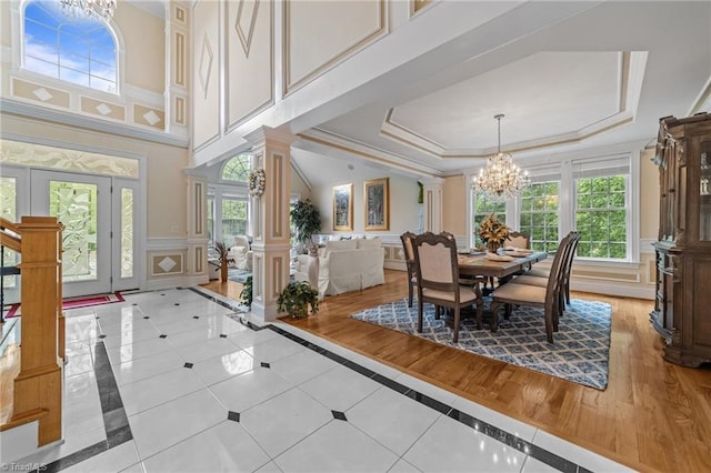dining area with inlaid floor details, ornate columns, a raised ceiling, a chandelier, and a decorative wall