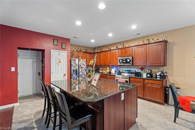 kitchen with stainless steel appliances, dark stone countertops, a center island with sink, and a kitchen bar