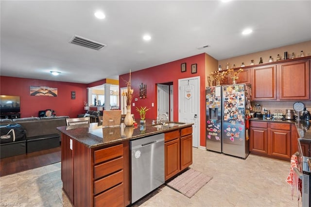 kitchen with sink, dishwasher, dark stone countertops, fridge with ice dispenser, and a center island with sink