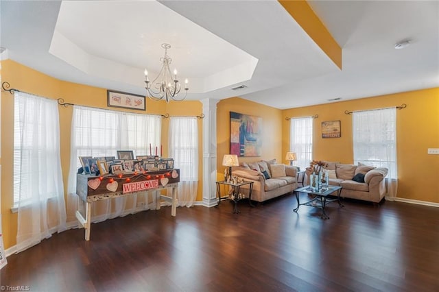 living room with ornate columns, dark hardwood / wood-style floors, an inviting chandelier, and a tray ceiling