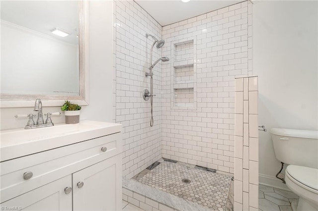 bathroom featuring toilet, tiled shower, tile patterned flooring, vanity, and ornamental molding