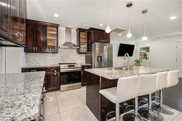kitchen featuring a sink, a kitchen breakfast bar, wall chimney exhaust hood, backsplash, and appliances with stainless steel finishes
