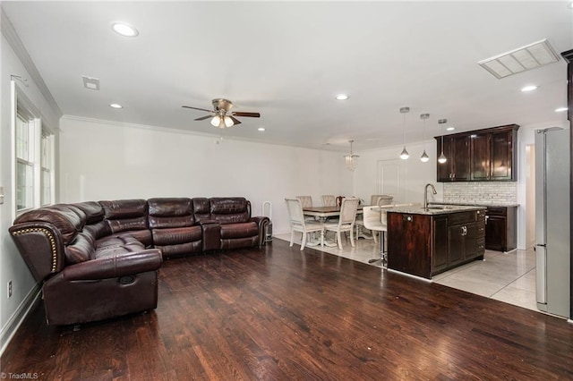 living room with crown molding, light wood-style floors, visible vents, and ceiling fan