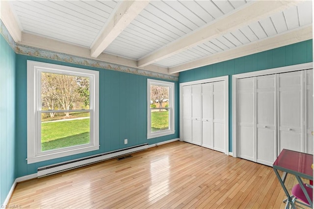 unfurnished bedroom featuring baseboard heating, multiple windows, two closets, and beam ceiling