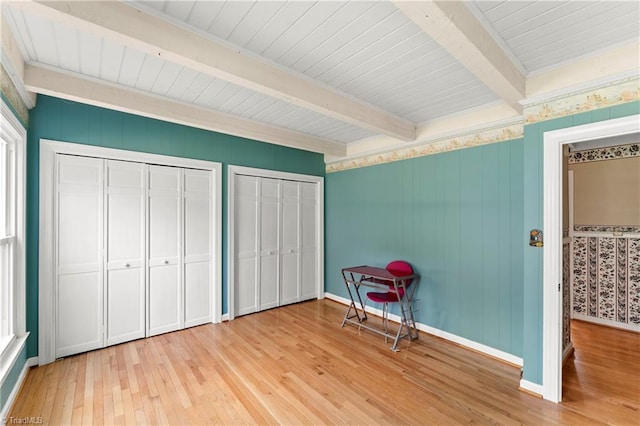 unfurnished bedroom with beamed ceiling, light wood-type flooring, and multiple closets