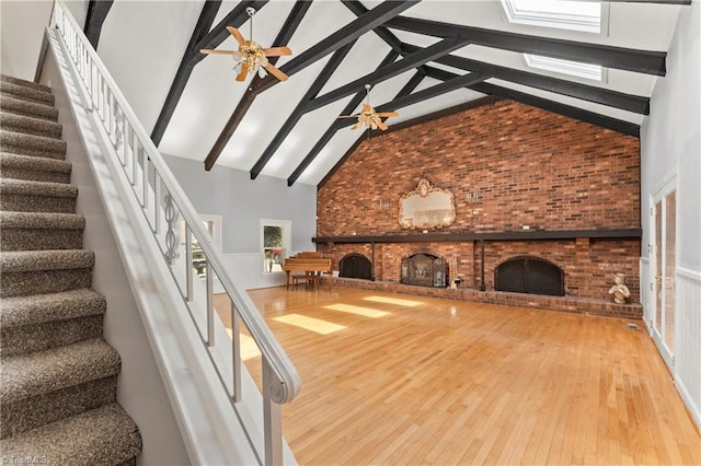 unfurnished living room featuring ceiling fan, wood-type flooring, high vaulted ceiling, beamed ceiling, and a fireplace