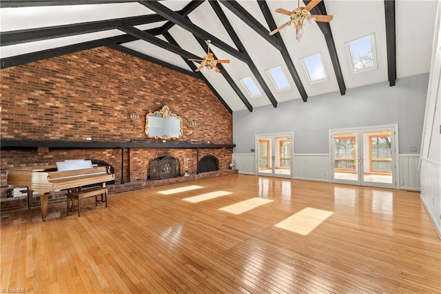 unfurnished living room with high vaulted ceiling, light hardwood / wood-style flooring, a skylight, ceiling fan, and a fireplace