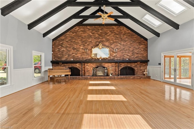 unfurnished living room featuring a skylight, high vaulted ceiling, ceiling fan, and light hardwood / wood-style flooring