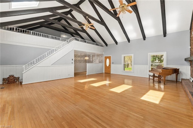 unfurnished living room with beamed ceiling, hardwood / wood-style floors, high vaulted ceiling, and ceiling fan