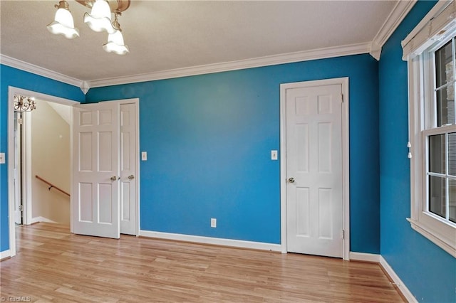 empty room with a notable chandelier, light hardwood / wood-style floors, and crown molding