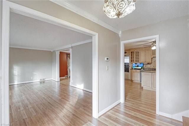 empty room featuring ceiling fan with notable chandelier, light wood-type flooring, and ornamental molding