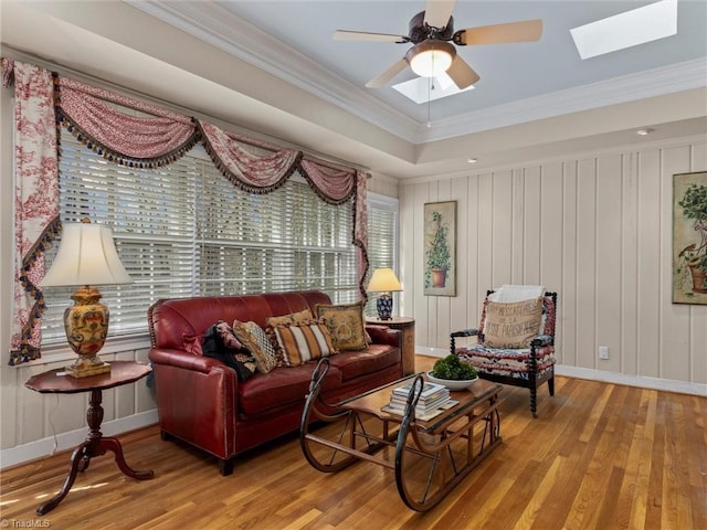 living area with ornamental molding, a skylight, a ceiling fan, and wood finished floors