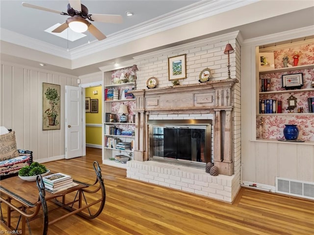 living area with visible vents, ceiling fan, ornamental molding, a fireplace, and wood finished floors