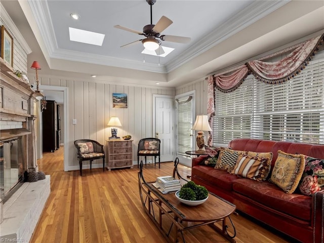 living room with ceiling fan, light wood-type flooring, a skylight, and crown molding