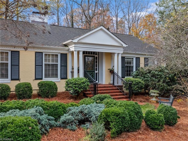 greek revival inspired property with brick siding, roof with shingles, and a chimney