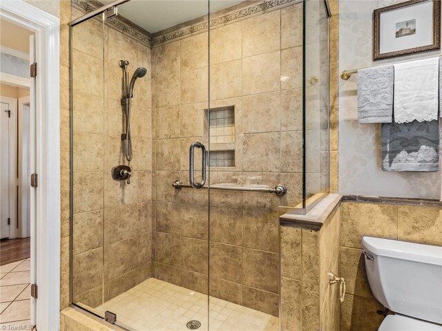 full bathroom with toilet, tile walls, a stall shower, and wainscoting