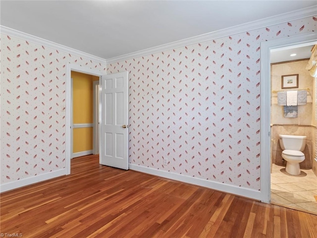 spare room with wallpapered walls, crown molding, and wood finished floors