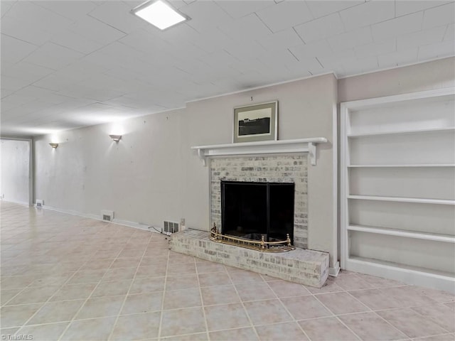 unfurnished living room featuring tile patterned floors, built in features, a brick fireplace, and visible vents