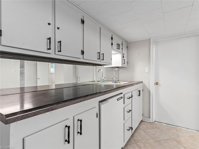 kitchen with dark countertops, light tile patterned floors, white cabinetry, and a sink