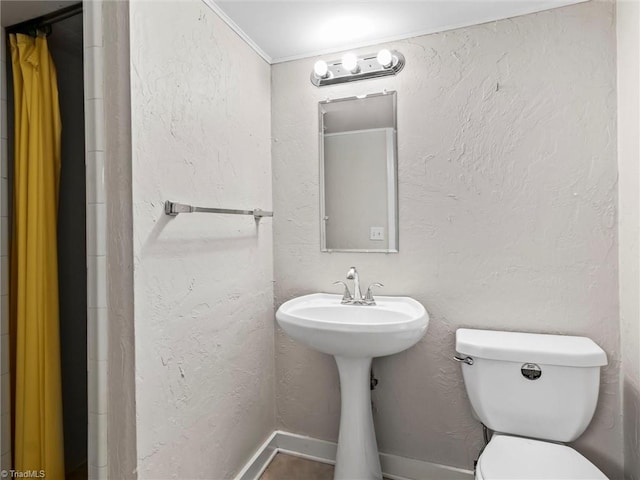 bathroom with toilet, baseboards, and a textured wall